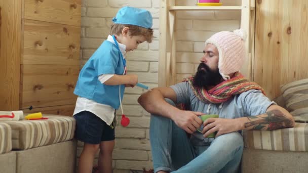 Garçon sous la forme d'un médecin fait une piqûre à un homme barbu. C'est très important. Charmant petit garçon en robe d'hôpital fait un vaccin pour son père qui fait une grimace . — Video