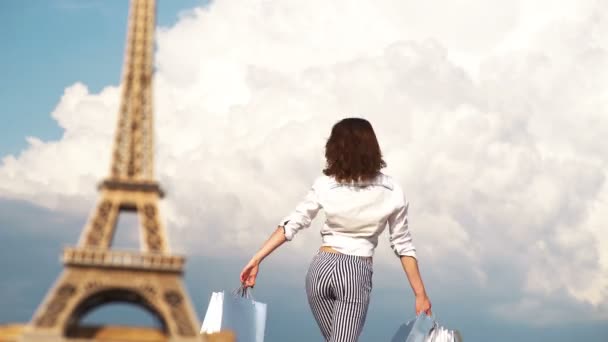 Chica con paquetes en el fondo del cielo y la torre eiffel. Una hermosa mujer va de compras a París. compras en París, mujer de moda cerca de la Torre Eiffel en Francia, Europa . — Vídeo de stock