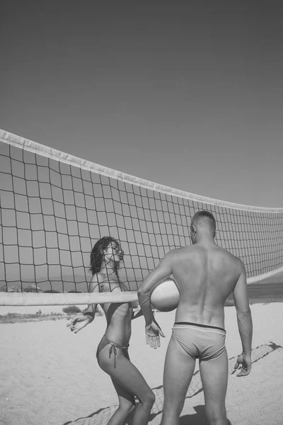 スポーティなアクティブなカップルはバレーボール ・ ネットの近くに立つ、夏の日のゲームをプレイします。カップルは楽しくバレーボールをプレーします。ビーチ バレーボール コンセプト。男女合わせて、強く、健康なビーチでスポーツをやって. — ストック写真