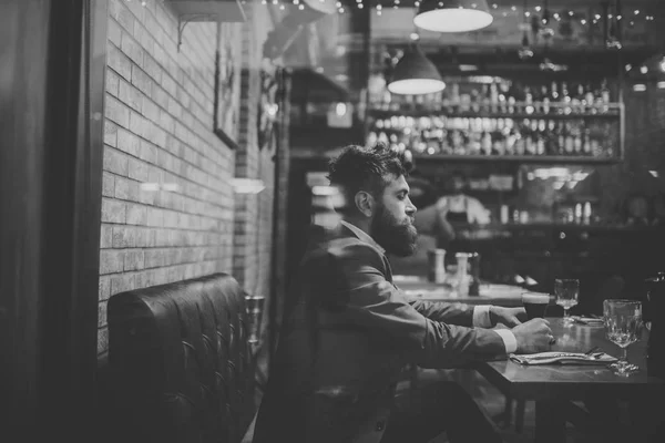 Bearded man rest in restaurant with beer glass. serious bar customer sit in cafe drinking ale. Date meeting of hipster awaiting in pub. Beer time. Businessman with long beard drink in cigar club.