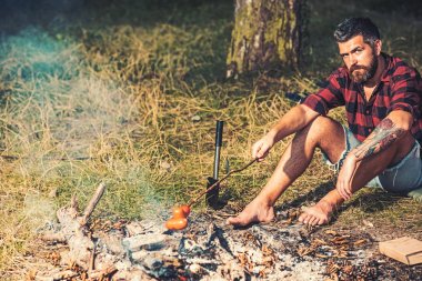 Ormanda kamp yapan yalnız bir gezgin. Adam ateşli sosis kızartmak için. Ormanda çim oturan Barefoot adam