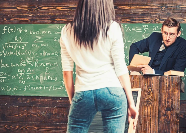 Učitel při pohledu přes své brýle na krásný mladý student stojící před pódium. Pohled zezadu mladá dívka — Stock fotografie