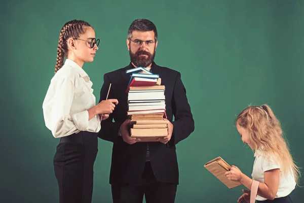 Back to school and home schooling. Teacher man and girls hold book pile at school. Literature lesson and reading grammar book. School time of sisters and father in library. Education in knowledge day — Stock Photo, Image