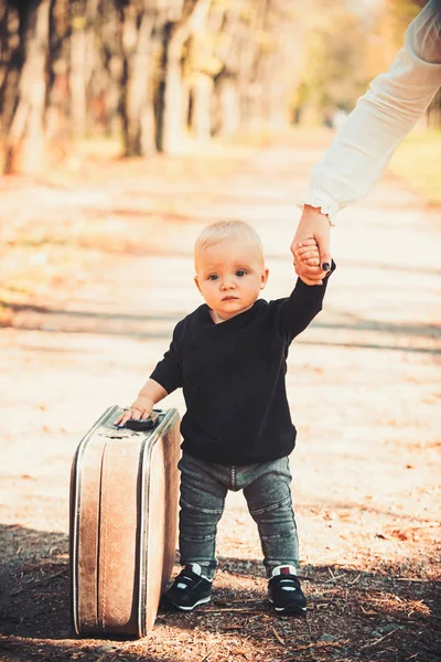 Reisendes Kind trägt Koffer auf Naturlandschaft. Junge reist mit Vintage-Tasche mit der Hand der Mutter — Stockfoto