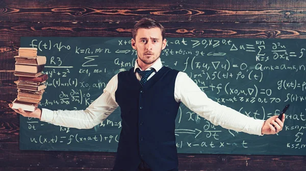 Balance between technology and knowledge, modern education concept. Blond guy in suit holding his hands like scales with pile of books in one hand and a phone in another — Stock Photo, Image