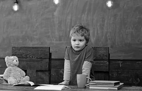 로 심각한 얼굴 서 어두운 나무 테이블의 뒤에 작은 소년. 테이블에 기대어 집중된 꼬마입니다. 아이 교사가 되길 — 스톡 사진