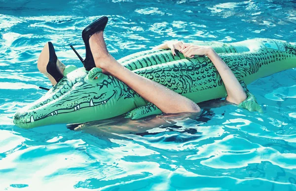 Piernas femeninas sostienen colchón en la piscina. piernas de niña abrazar cocodrilo inflable en el agua de la piscina —  Fotos de Stock