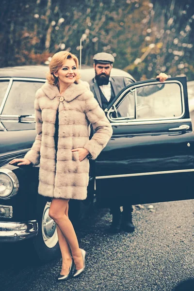 Retro collection car and auto repair by mechanic driver. Bearded man and sexy woman in fur coat. Escort of girl by security. Couple in love on romantic date. Travel and business trip or hitch hiking. — Stock Photo, Image