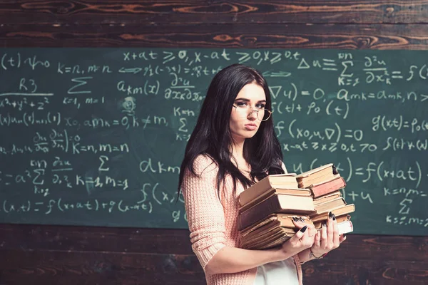 Serieuze jonge vrouwelijke student voor examens. Brunette meisje in glazen uitvoering twee stapels zware boeken — Stockfoto
