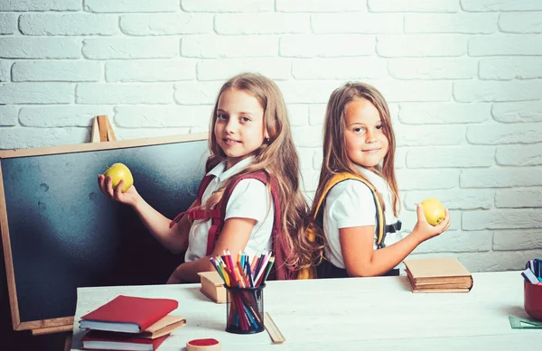 Kleine meisjes eet appel bij de lunchpauze. Gelukkig schoolkinderen op les in 1 september. Vriendschap van kleine zusters in de klas op de dag van de kennis. Terug naar school en huis het scholen. Schooltijd van meisjes — Stockfoto