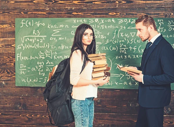 Brunette vrouwelijke student staande voor groen bord met hoopje van boeken en grote rugzak. Professor kijken mooi meisje in de klas — Stockfoto