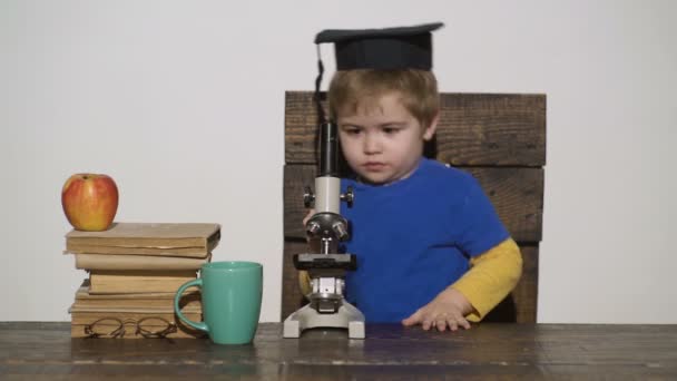 Il ragazzo guarda al microscopio. Concetto di Wunderkind - bambino piccolo intelligente, bambino di scienziato che lavora con microscopio, computer portatile. Concetto di scuola primaria. In primo luogo interessati a studiare, imparare, istruzione. Scienza. . — Video Stock