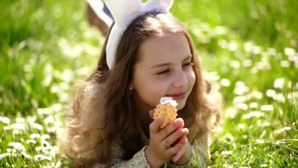 Kind met schattige bunny oren liggen op de weide. Meisje op jacht naar de Easter egg in lentetuin op Paasdag, traditionele feest. Pasen feest concept. Schattig kind lag op gras met ei in handen. — Stockvideo