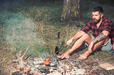 Hippi ile sakal kızartma sosis yanıyor. Sakallı adam aşçı gıda şenlik ateşi. Ekose gömlekli adam rahatla doğa üzerinde. Turist kamp keyfini çıkarın. Yaz tatil kavramı. Kamp ve yemek yemek, vintage