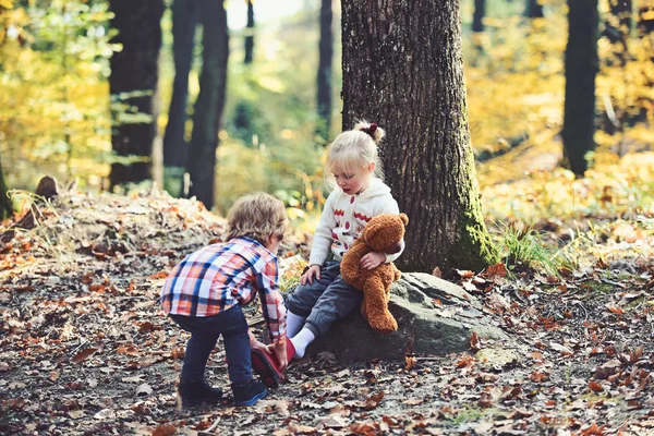 Kisfiú tesz cipőt a lány lábára. Brother Súgó nővére tesz a piros csizma. Segítő kéz koncepció. Gyermekek őszi erdőben sétálni készül. Gyermekkori barátság, a szeretet és a bizalom — Stock Fotó