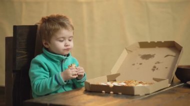 Çocuk bir ahşap arka plan üzerinde pizza yemek. Lezzetli pizza. Küçük çocuk bir dilim pizza sahip. Pizza tarafından bir ısırık alarak aç çocuk. Beslenme kavramı.