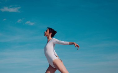 Güzel ve zarif. Sevimli bale dansçısı. Mavi gökyüzünde dans eden genç balerin. Dans giyen güzel bir kız. Klasik bale sanatı pratik. Konser performans dansı. Klasik dans stili