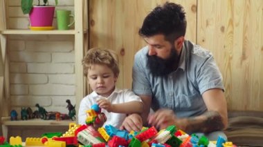 Adam ve çocuk birlikte ahşap duvar arka plan üzerinde oynamak. Ailesi ve çocukluk kavramı. Baba ve çocuk plastik blokları inşa. Baba ve oğul ciddi yüzü olan oyuncak tuğla ile renkli yapılar oluşturmak.