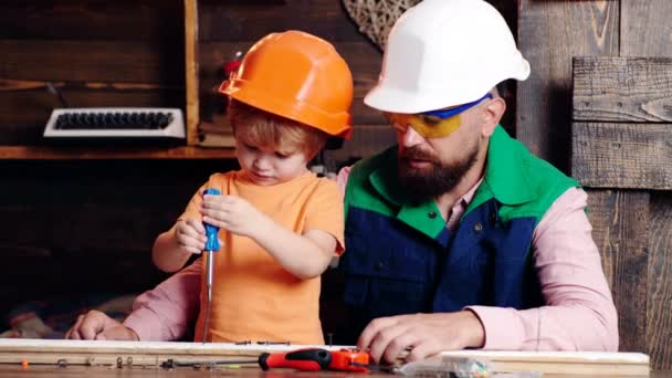 Garçon occupé à casque de protection apprendre à tourner les vis avec tournevis avec papa. Atelier et concept bricoleur. Papa et fils travaillent avec des outils. Parent avec un fils occupé. Petit garçon utilisant un tournevis . — Video