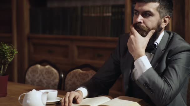 Un hombre barbudo reflexivo lee un libro en la biblioteca mientras está sentado a la mesa. Un hombre inteligente en la biblioteca. Elite inteligente y concepto de educación. Interior clásico vintage . — Vídeos de Stock