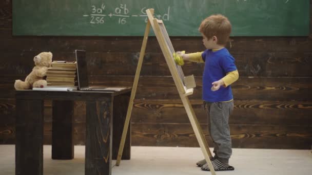Close-up van een jongen die schrijft met krijt op een bord. Kleine kunstenaar schildert op een houten achtergrond. Concept van beeldende kunst. Onderwijs en speel concept voor jonge kinderen. Creativiteit en educatieve kunst. — Stockvideo