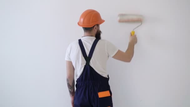 Borstel of roller met witte verf. Thuis DIY renovatieproces. Achteraanzicht van de schilder man verf de muur met verfroller geïsoleerd op witte kamer. Grappige schilder glimlacht en houdt zijn vinger omhoog. — Stockvideo