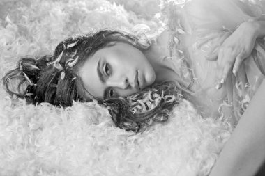 Sakin yüzündeki kız tüyler ve kabarıklıklarla kaplı bir şekilde yatağa uzandı. Havadarlık kavramı. İhale pijama rahatlatıcı uzun saçlı kadın. Şeffaf mavi gecelik lady tüyleri yığını içinde yatakta yatıyordu.