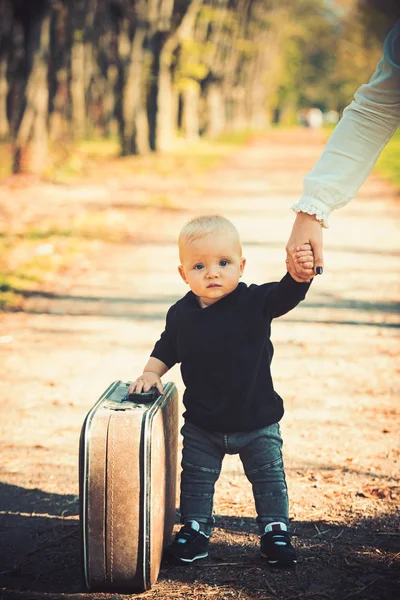 Niño viajero llevar bolso vintage con la mano de las madres, la infancia. Viaje infantil con maleta retro en paisaje natural — Foto de Stock