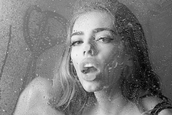 Window with water drops before girl with makeup. Shower and hygiene spa treatment. Sexy woman behind plastic sheet with water drops. Rain drops on window glass in heart shape. Fashion beauty and love