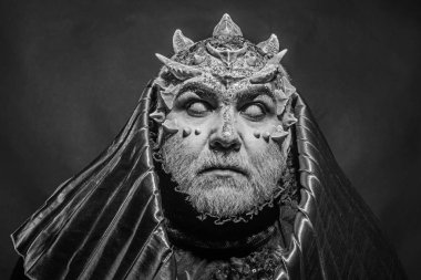 Beyaz sakallı komuta sizde canavar gibi giyinmiş. Adam dikenler veya siğiller ile yüz pırıltılar ile kaplı. Siyah zemin üzerine altın kukuleta ile iblis. Fantezi kavramı. Uzaylı, iblis, büyücü makyaj.