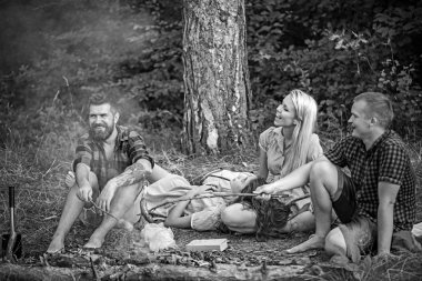 İki çiftler ormanda kamp. Ateşte sosis pişirme kırmızı oduncu gömlek içindeki adamlar. Gülümseyen arkadaş rahatlatıcı akşam kamp ateşi etrafında