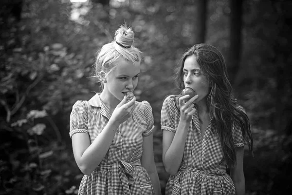 Camping in woods. Young women wandering in forest. Girls in vintage dresses eating juicy tomatoes