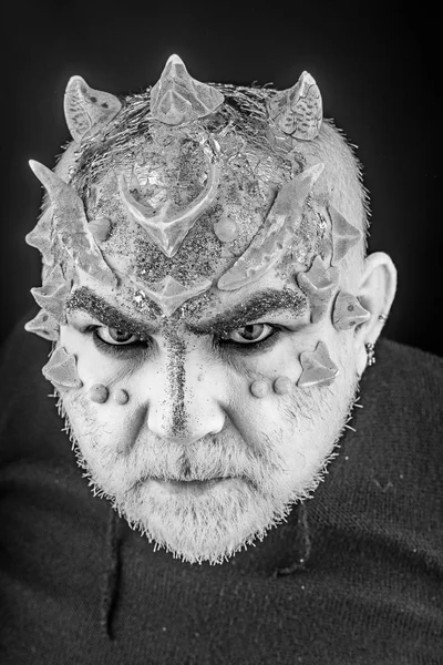 Head with thorns or warts, face covered with glitters, close up. Alien, demon, sorcerer makeup. Fantasy concept. Demon on serious face, black background. Senior man with beard, with monster makeup.