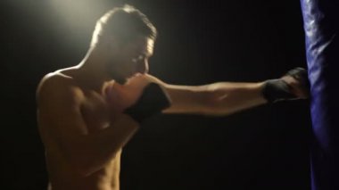 Yalnız boksör karanlık spor salonunda kum torbası vurur. Genç adam içeride eğitim ediyor. Spor salonunda güçlü bir atlet. Spor konsepti. Boxer kum torbasında darbeler üzerinde çalışıyor. Siyah arka planda yalıtılmış.