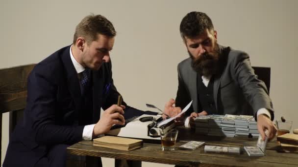 Illegal business concept. Men sitting at table with piles of money and typewriter. Company engaged in illegal business. Businessmen discussing illegal deal while drinking and smoking, white background — Stock Video