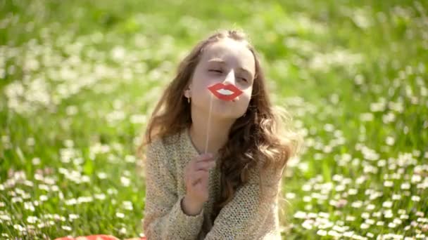 陽気な顔の女の子は、アウトドア レジャーをお過ごしください。ファッショニスタのコンセプトです。子供サングラス段ボール草原でのフォト セッションの唇を笑顔でポーズします。草地、緑の背景に芝生の上に座っている女の子. — ストック動画