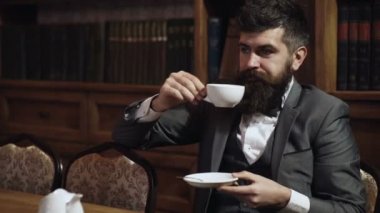 Lüks yaşam tarzı, başarı, zarafet, çay zamanı konsepti. Aristokrat lüks bir yerde oturur ve çay ya da kahve içer. Dolabında zarif takım elbiseli sakallı bir adam. Sakin yüzlü zengin adam çay saatinin tadını çıkarıyor..