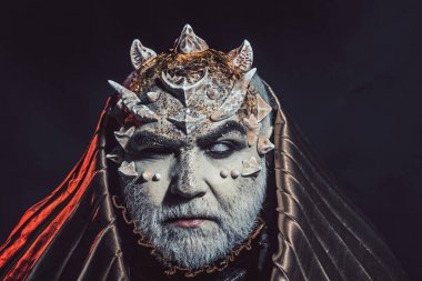 Beyaz sakallı komuta sizde canavar gibi giyinmiş. Adam dikenler veya siğiller ile yüz pırıltılar ile kaplı. Fantezi kavramı. Siyah zemin üzerine altın kukuleta ile iblis. Uzaylı, iblis, büyücü makyaj