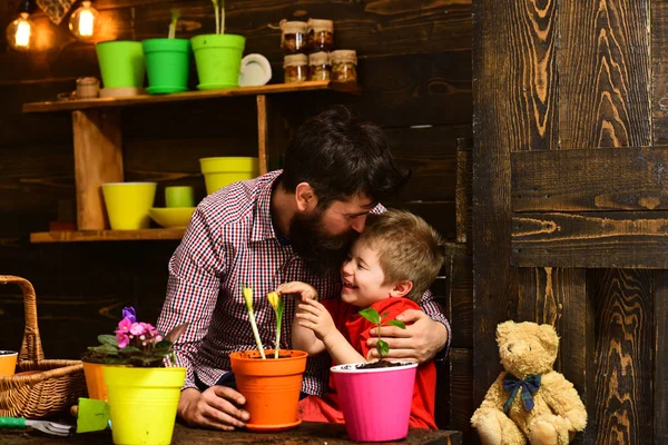 Family day. Greenhouse. happy gardeners with spring flowers. Father and son. Fathers day. Flower care watering. Soil fertilizers. bearded man and little boy child love nature. New flowers