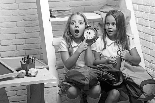 Tarde. Las chicas pequeñas conmocionadas muestran la hora del reloj. niños pequeños tarde a la escuela . — Foto de Stock