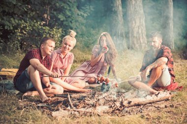 Tatilde kamp ve yemek pişirmek. Arkadaşlar ormandaki şenlik ateşinde piknik yapar. Erkekler ve kadınlar sosisleri ateşe verler. Erkek ve kız arkadaşlar kamp yemek keyfini çıkarın. İnsanlar yaz doğasında rahatlar