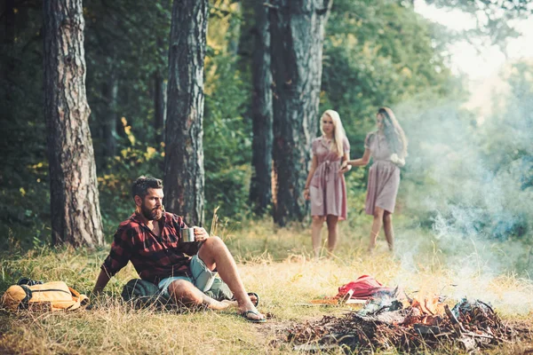 Concepto medioambiental. Un hombre reflexivo mirando llamas de fogata. Dos chicas descalzas explorando el bosque — Foto de Stock
