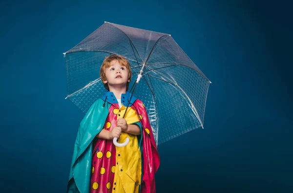 Χαρούμενο αγόρι με αδιάβροχο με πολύχρωμη ομπρέλα. Το παιδί στη βροχή. Χαριτωμένο αγοράκι προετοιμάζονται για το φθινόπωρο ηλιόλουστη μέρα. Χαριτωμένο μικρό παιδί αγόρι φορώντας το φθινόπωρο ρούχα την ημέρα του φθινοπώρου βροχή. — Φωτογραφία Αρχείου