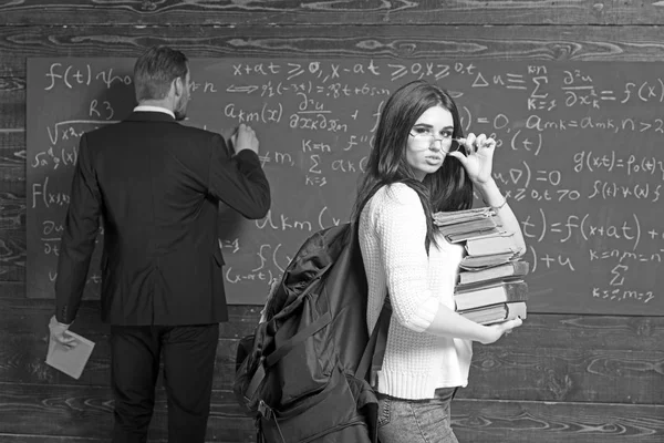 Brünette Studentin mit Bücherstapel im Hörsaal, während Professor Formel auf grüne Tafel schreibt — Stockfoto