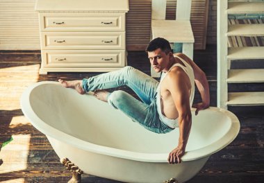 Banyo adam otur. Adam banyoda. Seksi maço kolsuz bluz ve kot moda. Fitness modeli güçlü beden sağlığı ile. Hijyen ve banyo kavramı