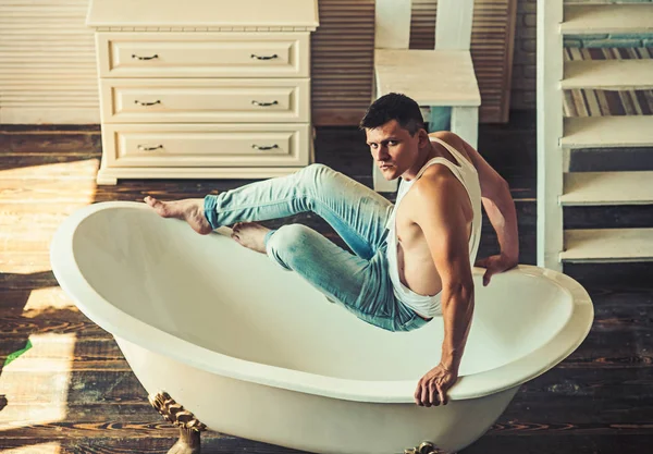 Tipul stă la baie. Bărbat în baie. Sexy macho în tank top și blugi moda. Modelul de fitness cu o sănătate corporală puternică. Conceptul de igienă și baie — Fotografie, imagine de stoc