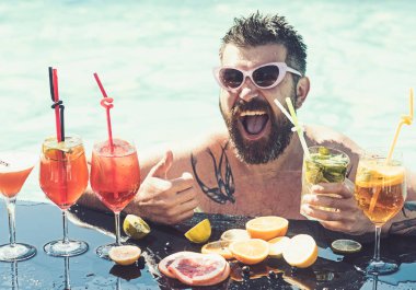 Yüzme havuzunun kenarında oturan yakışıklı bir adamın portresi. Model güneş gözlüğü giyiyor. Yanında tropik bir içki. Yaz tatili konsepti