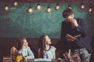 Sınıf arka planda öğretmen ve kız öğrenciler. Ev okullama ve okul konsepti geri. Gülümseyen yüzler ile çocuklar ve öğretmen. Kızlar ve sakallı adam masada oturup kitap okumak