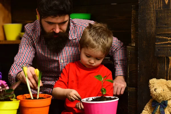 happy gardeners with spring flowers. man and little boy child love nature. Father and son. Fathers day. Flower care watering. Soil fertilizers. Family day. Greenhouse. Put everything under control