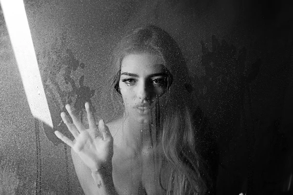 Fashion beauty and love. Rain drops on window glass in heart shape. Sexy woman behind plastic sheet with water drops. Shower and hygiene spa treatment. Window with water drops before girl with makeup